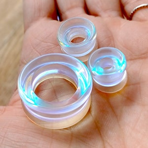 May include: Three iridescent clear acrylic ear gauges of different sizes. The gauges are round and have a smooth, polished finish.