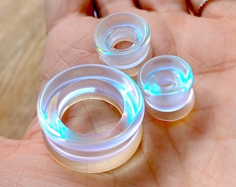 May include: Three iridescent clear acrylic ear gauges of different sizes. The gauges are round and have a smooth, polished finish.