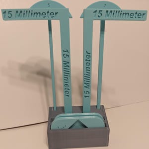 May include: A set of teal-colored 15-millimeter gauges with a gray storage box. The gauges have a T-shape design with the measurement clearly labeled. The box contains additional teal gauge pieces.
