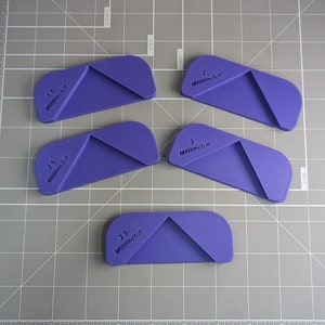 May include: Five purple plastic triangle-shaped rulers with measurements in millimeters. The rulers are 1.5, 2.5, 2, 3, and 3.5 millimeters.