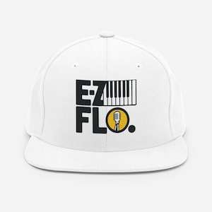 Op de afbeelding: Een witte baseball cap met een platte klep. De cap heeft de tekst "EZ FLO" in zwarte blokletters, een pianotoetsenbordafbeelding en een microfoonpictogram in een gele cirkel.