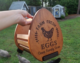 May include: Wooden egg-shaped egg holder with the words "Farm Fresh Eggs" and a hen illustration. The holder is held by a hand in a grassy outdoor setting with chickens.