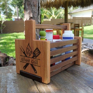 K&ouml;nnte beinhalten: Ein Grill-Caddy aus Holz mit einem Griff, personalisiert mit dem Namen "Albert Grill" und einem Design aus einem Spatel und einer Gabel, die &uuml;ber einer Flamme gekreuzt sind. Der Caddy hat vier F&auml;cher zum Verstauen von Grillwerkzeug und Gew&uuml;rzen.