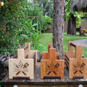 K&ouml;nnte beinhalten: Drei Grillwerkzeug-Halter aus Holz mit personalisierten Gravuren. Der erste Halter sagt "Fisher's BBQ", der zweite sagt "The Espinoza Family" und der dritte sagt "John's Grill".