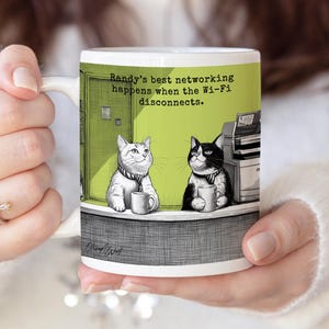 May include: White ceramic mug featuring a humorous cartoon of two cats in an office setting. The mug has the text "Randy's best networking happens when the Wi-Fi disconnects." The cats are holding mugs, and the background is a light green color.
