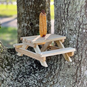 May include: A small wooden picnic table with a corn cob on top, mounted on a tree trunk.