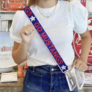May include: Blue and red striped adjustable shoulder strap with white stars and the text "GS GO MUSTANGS".