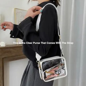 May include: A clear plastic purse with a white frame and a white adjustable strap. The purse has a clear view of the inside, which is filled with a patterned fabric.