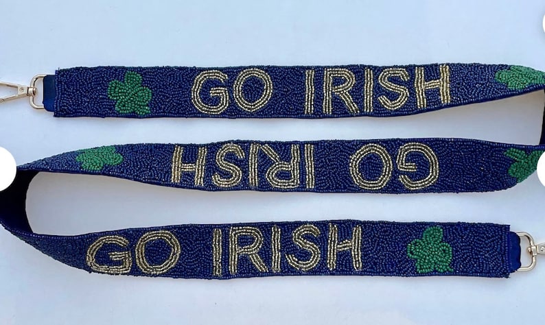 Może przedstawiać: Niebieski pasek z koralik&oacute;w z złotymi koralikami tworzącymi napis "GO IRISH" i zielonymi zawieszkami w kształcie koniczyny.