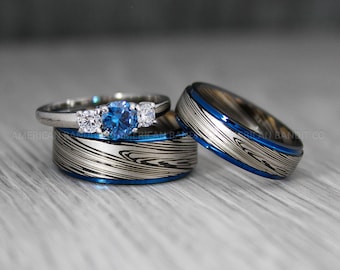 May include: A set of three wedding bands with a blue and silver patterned design. The center band features a three-stone ring with a blue center stone and two smaller white stones.