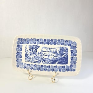 May include: A rectangular cream-colored ceramic tray featuring a blue transferware landscape scene in the center, depicting a castle and trees. The border is decorated with a repeating pattern of blue leaves and small flowers on a ribbed edge.