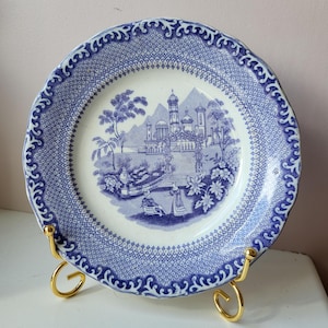 Może przedstawiać: Błękitno-biały talerz porcelanowy z dekoracyjnym wzorem przedstawiającym zamek i drzewa. Talerz ma falisty brzeg i błękitno-biały wzór wokół krawędzi.