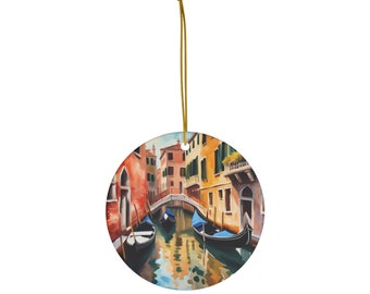 May include: A round ceramic ornament featuring a watercolour painting of a canal in Venice, Italy. The painting depicts colourful buildings lining the canal, with gondolas floating on the water. The ornament has a gold string for hanging.