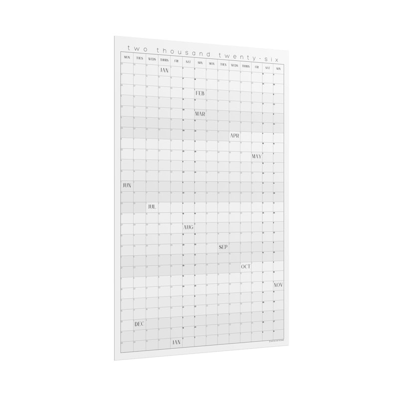 Op de afbeelding: Een grote, rechthoekige wandkalender voor het jaar 2026. De kalender is wit met een raster van grijze vierkanten voor elke dag. Maanden staan bovenaan en aan de zijkant. De tekst "two thousand twenty-six" staat bovenaan.