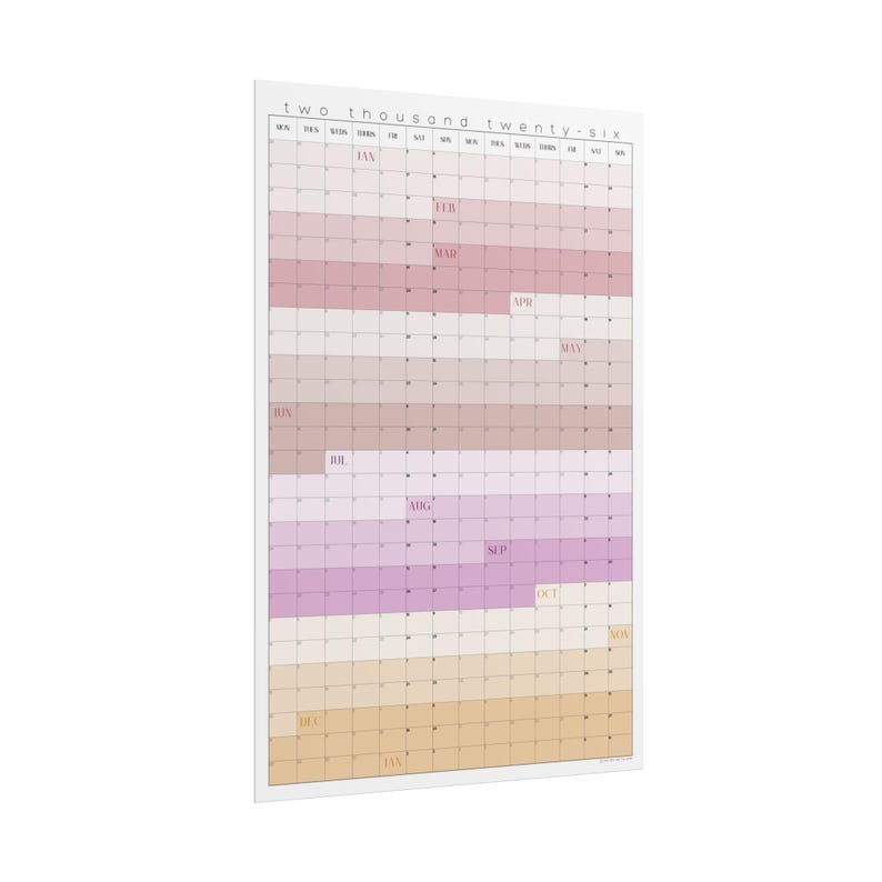 Op de afbeelding: Een grote wandkalender voor het jaar 2026, met een rasterindeling en maandelijkse blokken. De kalender heeft een witte rand en een kleurenschema van roze, paars en beige. De tekst "two thousand twenty-six" staat bovenaan.