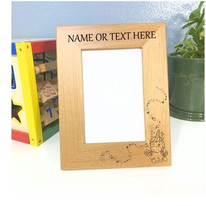 May include: A light-colored wooden picture frame with the text "NAME OR TEXT HERE" at the top. A whimsical unicorn design is etched on the lower right corner. The frame is empty, ready for a photo.