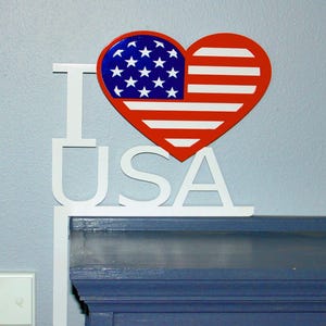 May include: A patriotic wall decoration featuring a red, white, and blue heart-shaped design of the American flag. The words "I USA" are displayed in white, creating a decorative piece for expressing national pride.