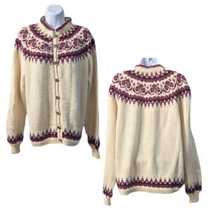 Könnte beinhalten: Ein cremefarbener Cardigan mit einem burgunderfarbenen und weißen Muster. Der Cardigan hat einen Knopfschließe und lange Ärmel.