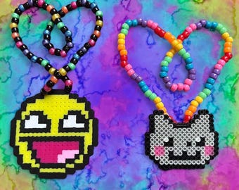 May include: Two necklaces made of colorful plastic pony beads arranged in heart shapes. One pendant is a yellow, black, and white pixelated face with a wide grin. The other pendant is a gray, black, and pink pixelated cat face with whiskers.