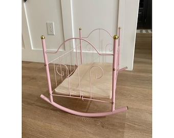 Culla a dondolo vintage in metallo rosa con cuscino, ideale per bambole.