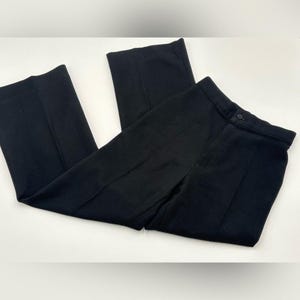 May include: A pair of black pants with a button closure and a straight leg design. The pants are made of a solid black fabric and are laid flat on a white surface. The pants appear to be new and unworn.