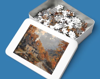 Puede incluir: Una caja blanca con la tapa abierta, que revela un rompecabezas completado. El rompecabezas representa una pintura de una casa en un bosque con hojas de otoño.