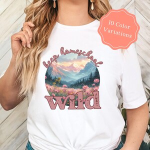 May include: White t-shirt with a round graphic featuring a mountain landscape and the words "keep homeschool wild" in pink. The shirt also has a peach-colored tag that says "10 Color Variations".