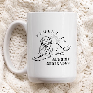 Puede incluir: Taza de cerámica blanca con una ilustración negra de un Golden Retriever y el texto "Fluent in Sunrise Serenades". La taza tiene un asa grande. El fondo es una tela blanca texturizada.