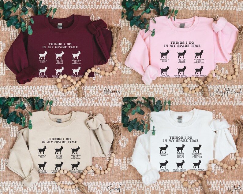 May include: Four sweatshirts in maroon, light pink, sand, and white are displayed. Each sweatshirt has the text "THINGS I DO IN MY SPARE TIME" with goat illustrations. The sweatshirts are on a textured surface with decorative beads.