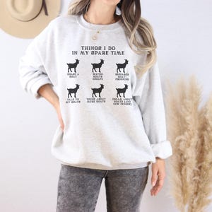 May include: A light gray sweatshirt with the text "THINGS I DO IN MY SPARE TIME" and goat illustrations. The text includes phrases like "GRAZE A GOAT", "WATCH GOATS ESCAPE", and "TALK TO MY GOATS".