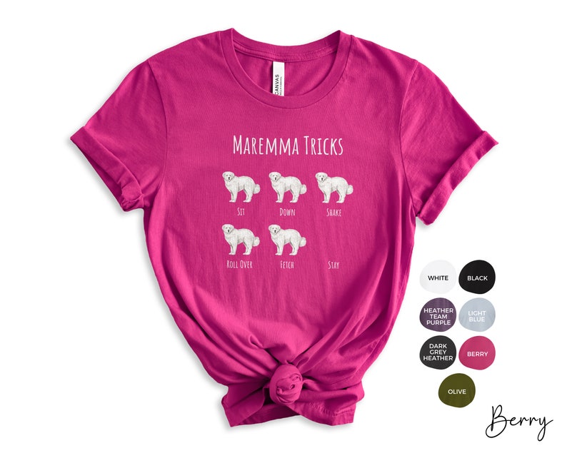 Pode incluir: Uma camiseta rosa com o texto "MAREMMA TRICKS" e ilustra&ccedil;&otilde;es de um c&atilde;o branco realizando v&aacute;rios truques, incluindo sentar, deitar, sacudir, rolar, buscar e ficar.