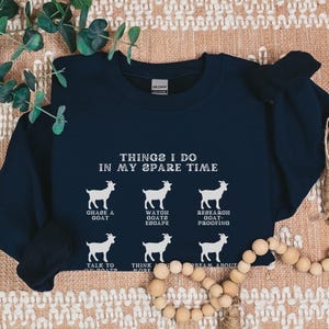 May include: Navy blue sweatshirt with white text and goat illustrations. The text reads "THINGS I DO IN MY SPARE TIME" with phrases like "CHASE A GOAT" and "DREAM ABOUT GOATS". The word "Navy" is at the bottom right.