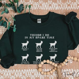 May include: Forest green sweatshirt with white text and goat illustrations. The text reads "THINGS I DO IN MY SPARE TIME" with phrases like "CHASE A GOAT" and "TALK TO MY GOATS". The sweatshirt is a crew neck.