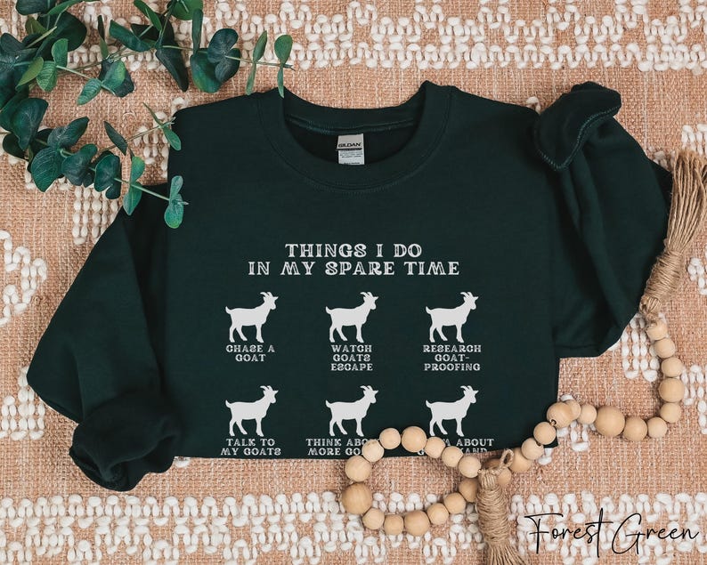 May include: Forest green sweatshirt with white text and goat illustrations. The text reads "THINGS I DO IN MY SPARE TIME" with phrases like "CHASE A GOAT" and "TALK TO MY GOATS". The sweatshirt is a crew neck.