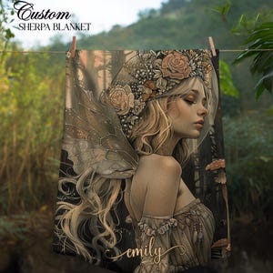 May include: Custom sherpa blanket featuring a detailed illustration of a fairy with blonde hair, floral crown, and delicate wings. The artwork has a soft, ethereal quality with muted tones and the name "emily" in cursive.