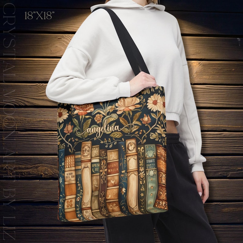 May include: A tote bag with a floral and book design. The bag is 18" x 18" and features a dark background with flowers and vintage-style book spines. The name "angelina" is written in cursive. The bag has a black strap.