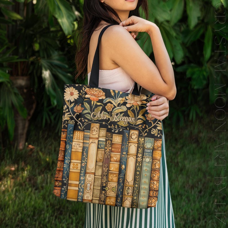 May include: Black tote bag featuring a floral design with orange and white flowers and the text "Ms. Keegan". The lower portion of the bag displays a stack of vintage-style books in various colors.