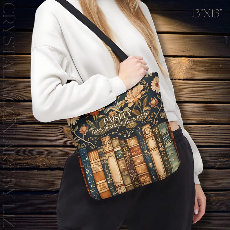 May include: A tote bag with a floral and book design. The bag features the text "Paisley Dark Romance Book Club" and measures 13 inches by 13 inches. The bag has a black strap and a dark background with floral and book illustrations.