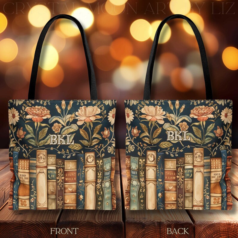 May include: A tote bag with a dark blue background featuring a floral design and a row of books. The bag has black handles and the initials "BKL" are displayed on the front and back. The floral design includes roses and other flowers.