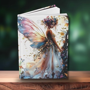 May include: A hardcover journal featuring a fantasy illustration of a fairy with colorful wings and a floral crown. The fairy is wearing a flowing gown and is surrounded by flowers and vines. The name "Reiley" is written on the cover.