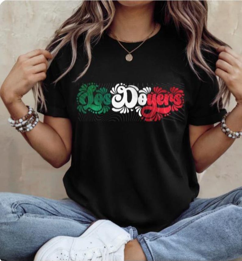 May include: A black t-shirt featuring a graphic of the words "Los Doyers" in green, white and red lettering. The lettering is stylised with swirls and floral designs.