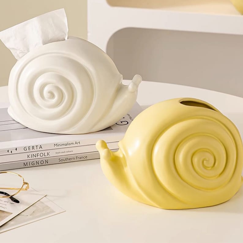 Puede incluir: Dos porta pa&ntilde;uelos de cer&aacute;mica con forma de caracol. Uno es blanco y el otro es amarillo.