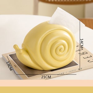Puede incluir: Un porta pa&ntilde;uelos de cer&aacute;mica amarillo con forma de caracol. El porta pa&ntilde;uelos mide 14 cm de alto, 21 cm de ancho y 13 cm de profundidad.