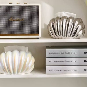 May include: Two ceramic tissue box covers shaped like seashells. One is silver and the other is iridescent white.