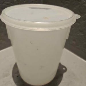 May include: A translucent white plastic cylindrical food storage container with a matching snap-on lid. The container features a slightly tapered body and a small tab on the lid for easy opening, providing a simple and functional design for storage.