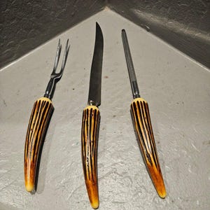 以下が含まれることがあります： フォーク、ナイフ、シャープナーの3つのヴィンテージ彫刻ツールセット。 各ツールは、茶色とクリーム色のストライプ模様のハンドルが付いています。 ブレードとスチールはシルバーカラーです。