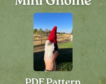Op de afbeelding: Een handgemaakte kabouter met een rode puntmuts, witte baard en zwart lichaam. De tekst "Mini Gnome" en "PDF Pattern" wordt in witte letters op een groene achtergrond weergegeven. De kabouter wordt in een hand gehouden tegen een blauwe lucht en een grasveld.