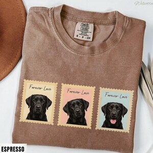 May include: Espresso-coloured t-shirt with three postage stamp designs. Each stamp features a black Labrador portrait and the words "Forever Love." The shirt has a crew neck and a Comfort Colors tag. The word "Espresso" is printed at the bottom.