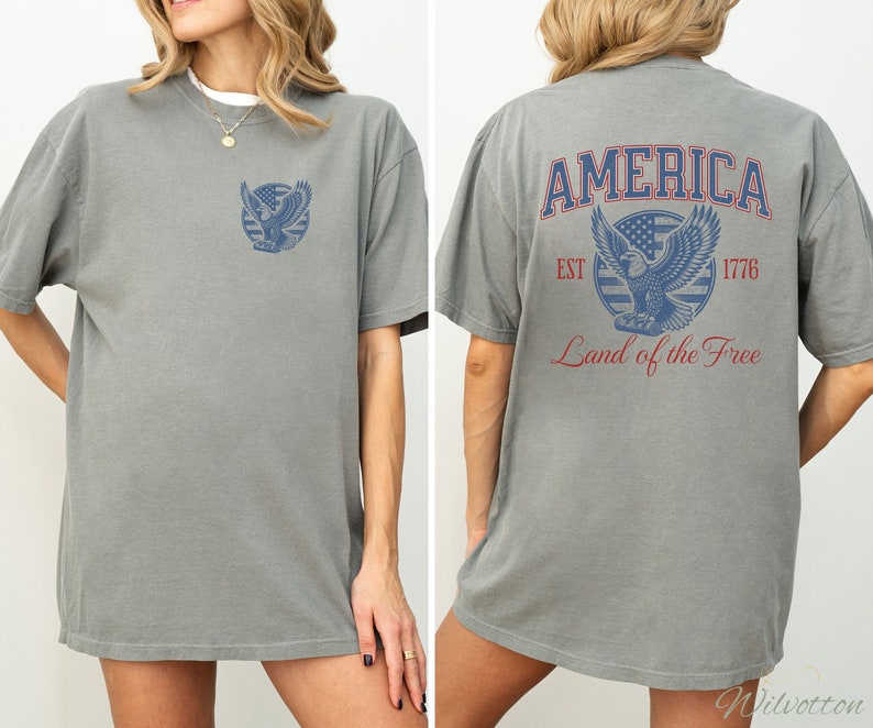 Puede incluir: Una camiseta gris con un gr&aacute;fico de estilo vintage de un &aacute;guila sosteniendo una pancarta con las palabras "AMERICA EST 1776 Land of the Free".