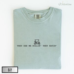 May include: A light blue t-shirt with a golf cart graphic and the text "They see me rollin' they hatin'".